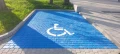 Parking dla niepełnosprawnych z niebieskiej kostki brukowej, biały symbol wózka inwalidzkiego. Miejsce parkingowe wydzielone dla osób z ograniczoną sprawnością ruchową, idealne do oznaczeń infrastruktury miejskiej, budowlanej i oznakowania parkingów