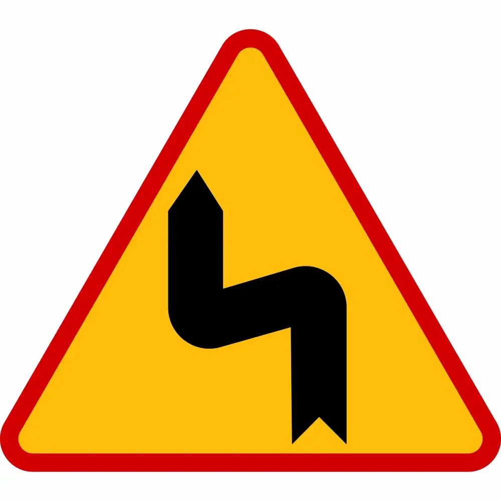 Znak drogowy ostrzegawczy A-4 niebezpieczne zakręty pierwszy w lewo. Odblaskowa folia I generacji, rozmiar 1200 mm. Żółty trójkąt z czerwoną ramką, pionowe oznakowanie drogowe poprawiające bezpieczeństwo ruchu. Producent Widrog