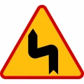 Znak drogowy ostrzegawczy A-4: niebezpieczne zakręty, pierwszy w lewo. Tablica drogowa o boku 900 mm z folią odblaskową I generacji. Polski znak drogowy typu A4 na żółtym tle w czerwonym obramowaniu