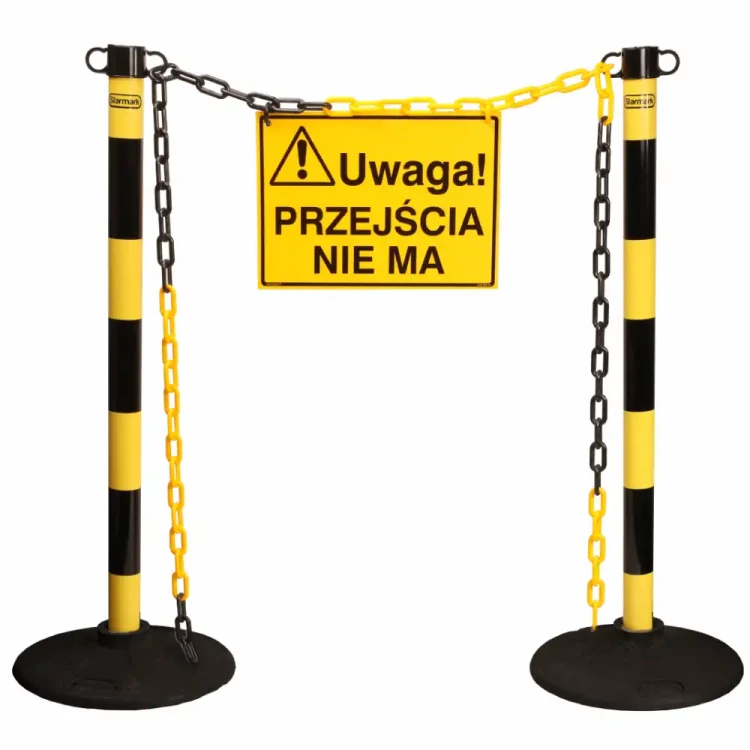 Dwa żółto-czarne słupki plastikowe z łańcuchem i tablicą „Uwaga! Przejścia nie ma” – bariera tymczasowa
